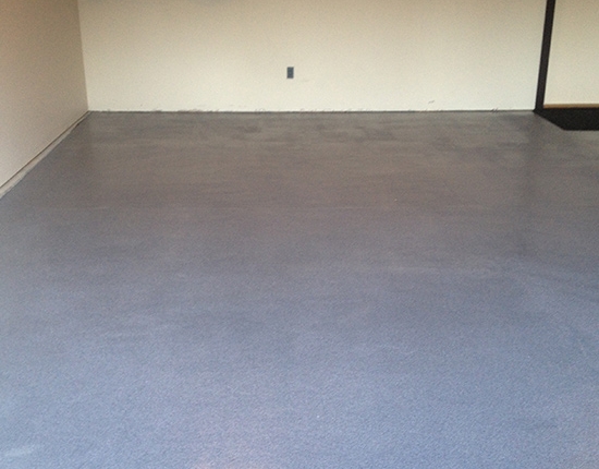 A clean, empty garage with smooth, shiny gray flooring finished with decorative concrete coatings for garage; two bicycles are mounted on the wall in the background.