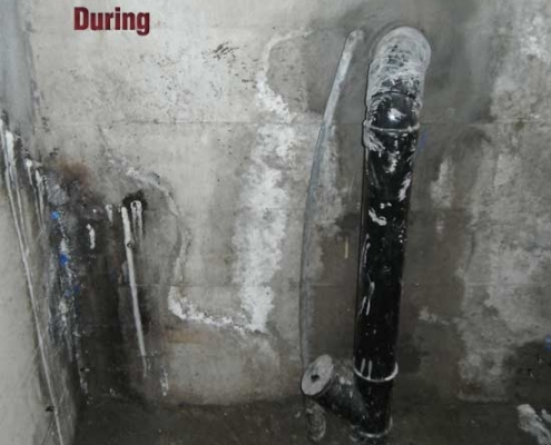A concrete wall and floor with exposed pipes and stains. The word "During" appears on the wall, indicating this is a construction or renovation phase where polyurethane grout injection may be underway. The area looks unfinished and dirty.