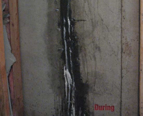 A concrete basement wall with a vertical crack being repaired using polyurethane grout injection; sealing material is visible along the crack, and the word "During" is printed in red at the bottom right.