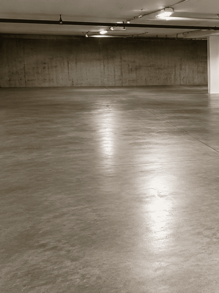cr-con-1 An empty, clean underground parking garage with smooth concrete floors, expertly maintained with cracked concrete repair, white pillars, overhead lights, and bare concrete walls.