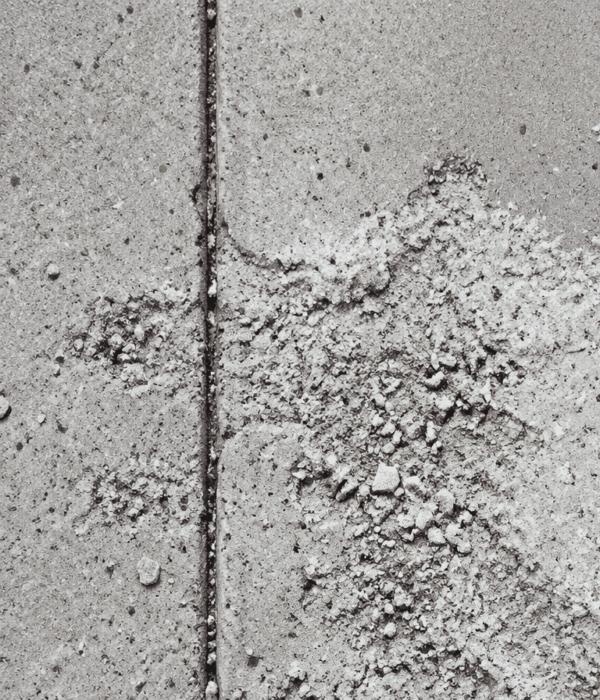 Powdery white dust and small debris scattered across a gray concrete surface, divided by a narrow line between the tiles, suggest recent efforts to repair concrete in the area.